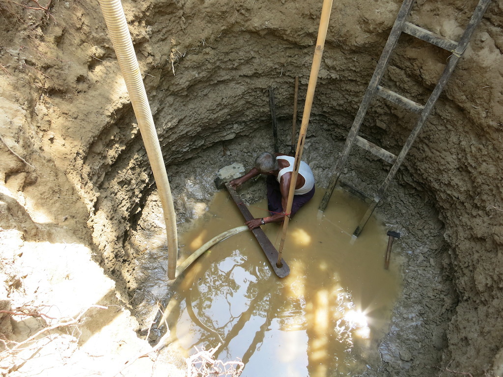 With extended radius and depth, the well is ready for lining. The first stone goes down…and is set right by the old well master.